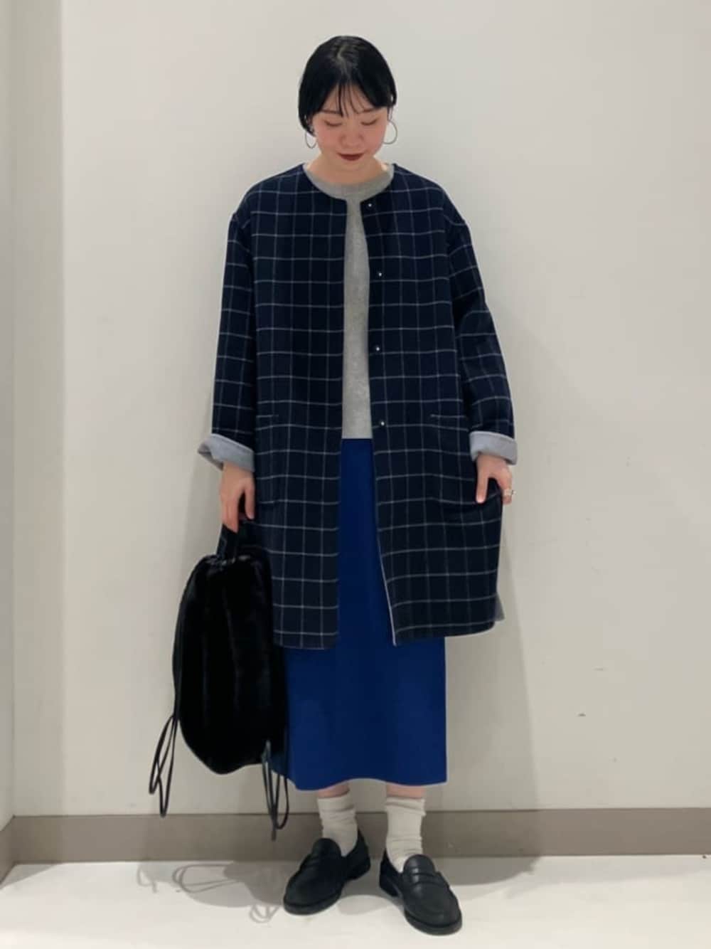グレー系のノーカラーコート、グレー系のニット/セーター、ブルー系のスカートを着用したレディースの秋コーディネートの1枚目の写真