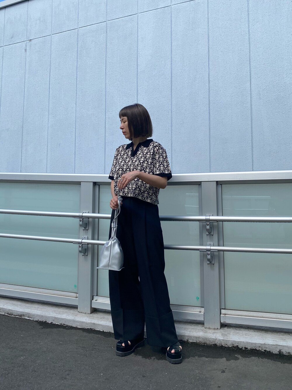 ブラック系のポロシャツ、グレー系のスラックス、ブラック系のサンダルを着用したレディースの春コーディネートの1枚目の写真