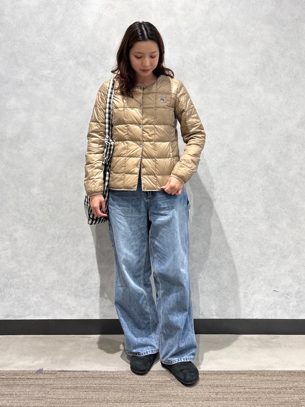 ブルー系のデニムパンツ、ベージュ系のダウンジャケット/コート、ホワイト系のトートバッグを着用したレディースの秋コーディネートの1枚目の写真