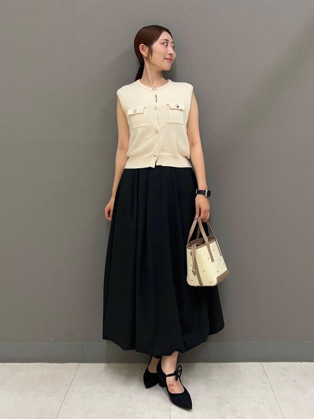 ブラック系のパンプス、ブラック系のスカート、ホワイト系のベストを着用したレディースの夏コーディネートの1枚目の写真