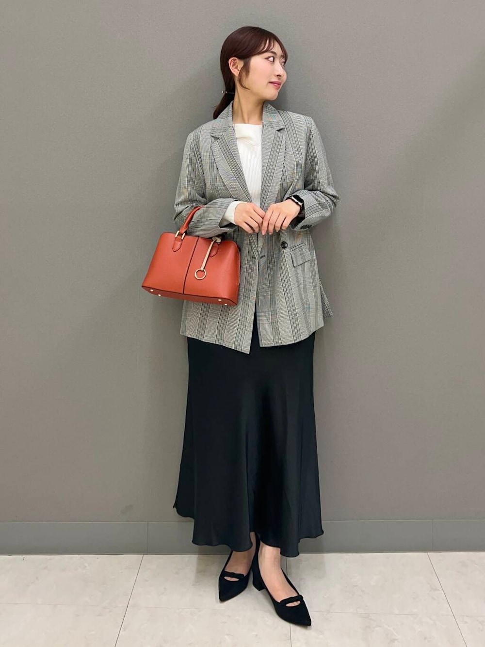 オレンジ系のハンドバッグ、ブラック系のパンプス、ブラック系のスカートを着用したレディースの春コーディネートの1枚目の写真