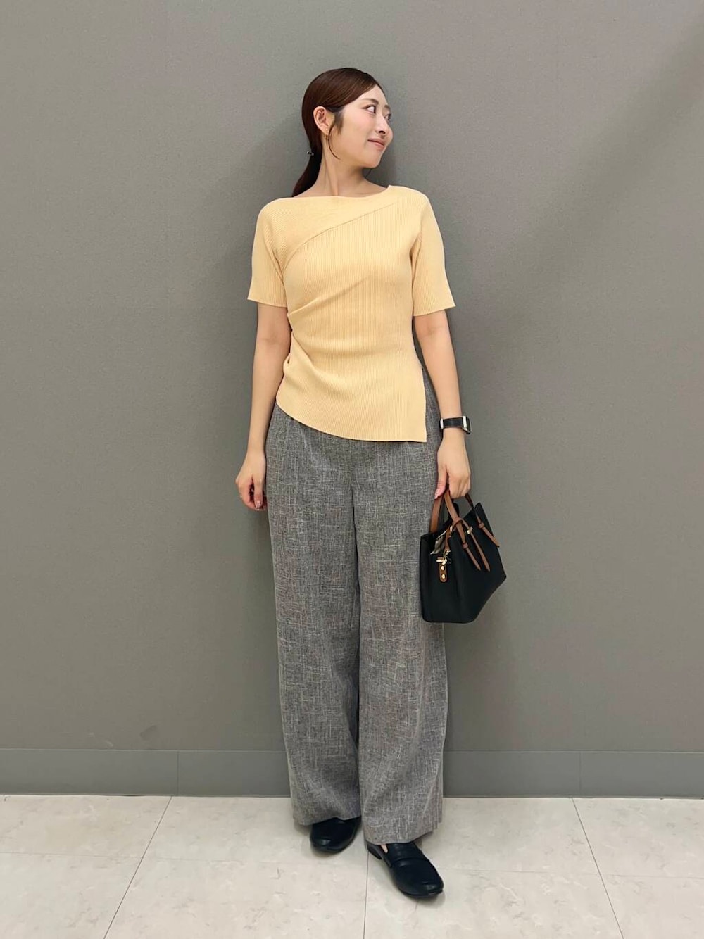 ブラック系のハンドバッグ、ブラック系のローファー、ベージュ系のニット/セーターを着用したレディースの夏コーディネートの1枚目の写真