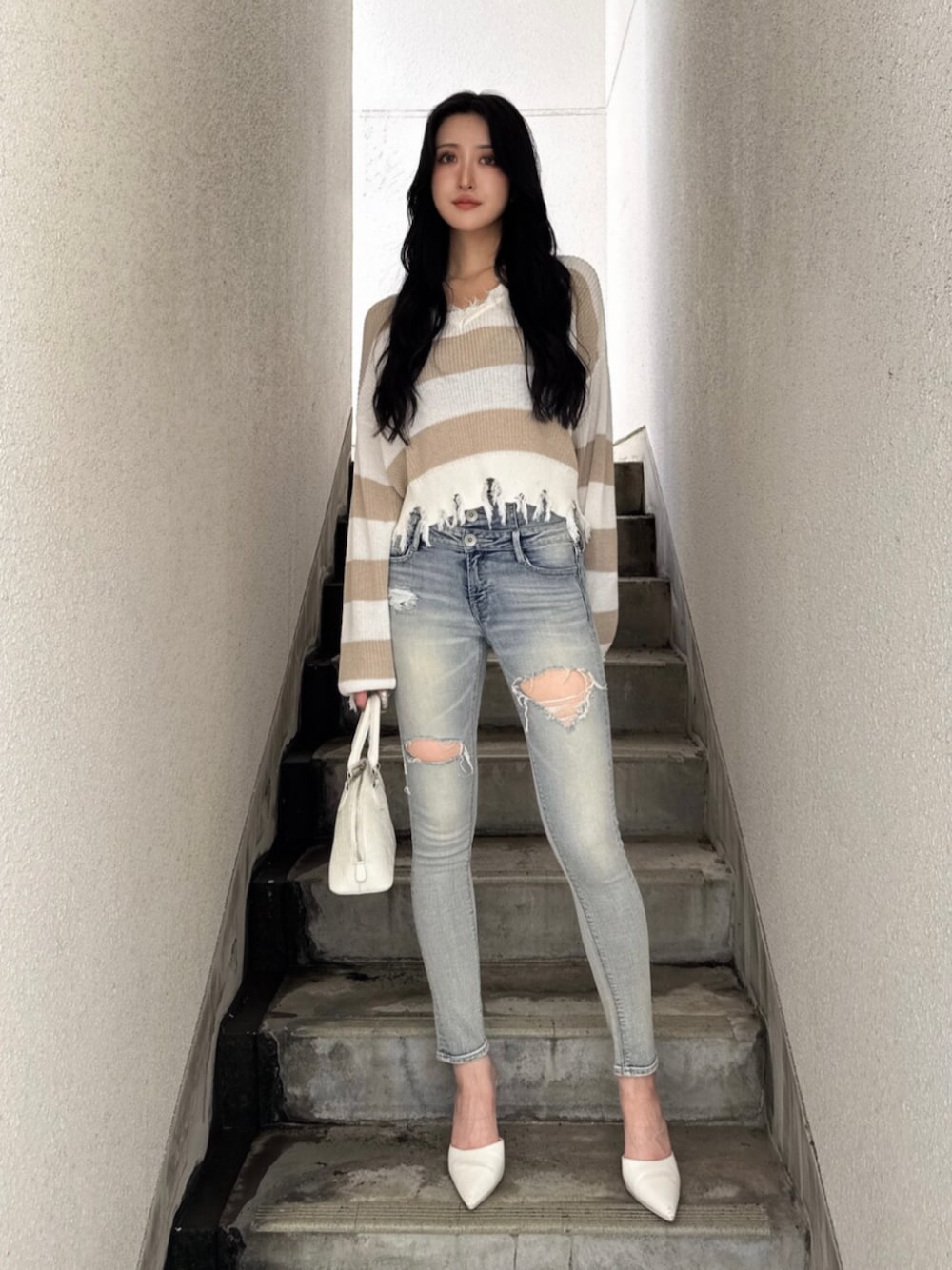 ベージュ系のニット/セーター、ブルー系のデニムパンツ、ホワイト系のハンドバッグを着用したレディースの夏コーディネートの1枚目の写真
