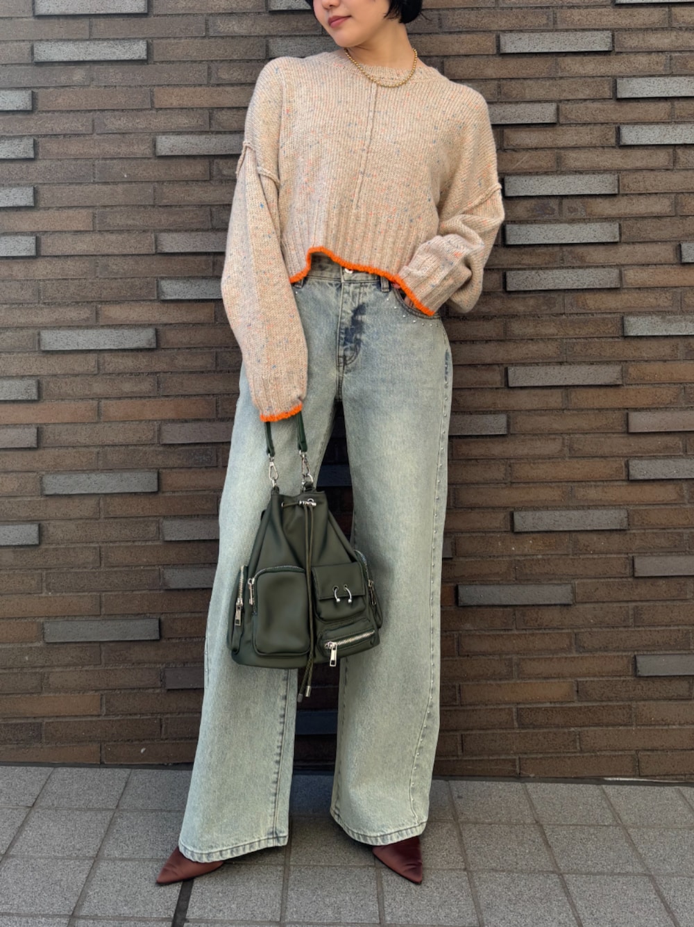 グリーン系のハンドバッグ、ベージュ系のニット/セーターを着用したレディースの冬コーディネートの1枚目の写真