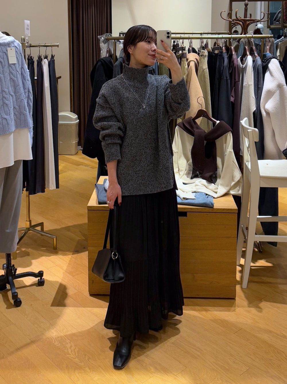 グレー系のニット/セーター、ブラック系のスカート、ブラック系のブーツを着用したレディースの秋コーディネートの1枚目の写真