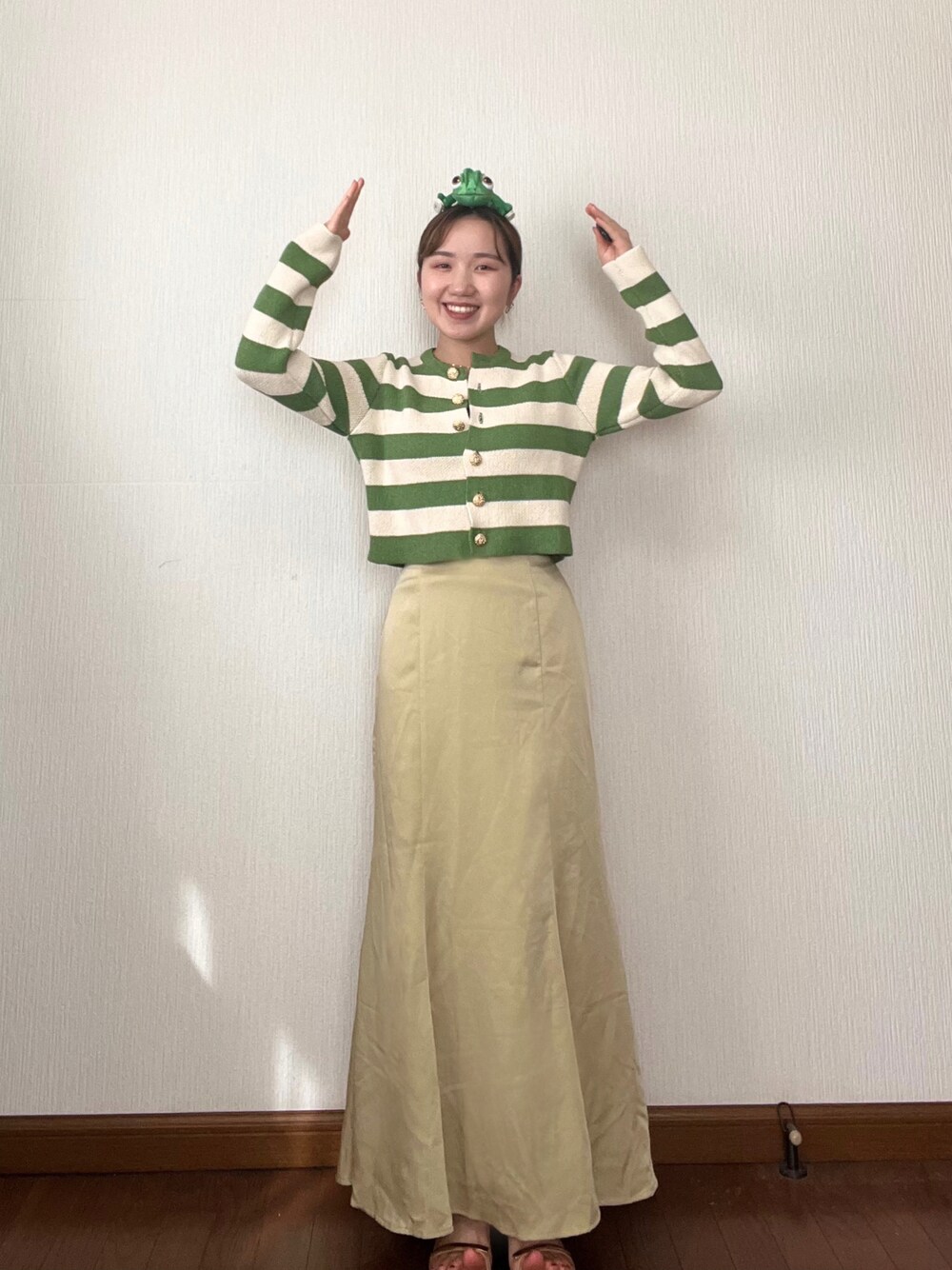 イエロー系のスカート、グリーン系のカーディガン/ボレロ、ベージュ系のサンダルを着用したレディースの秋コーディネートの1枚目の写真