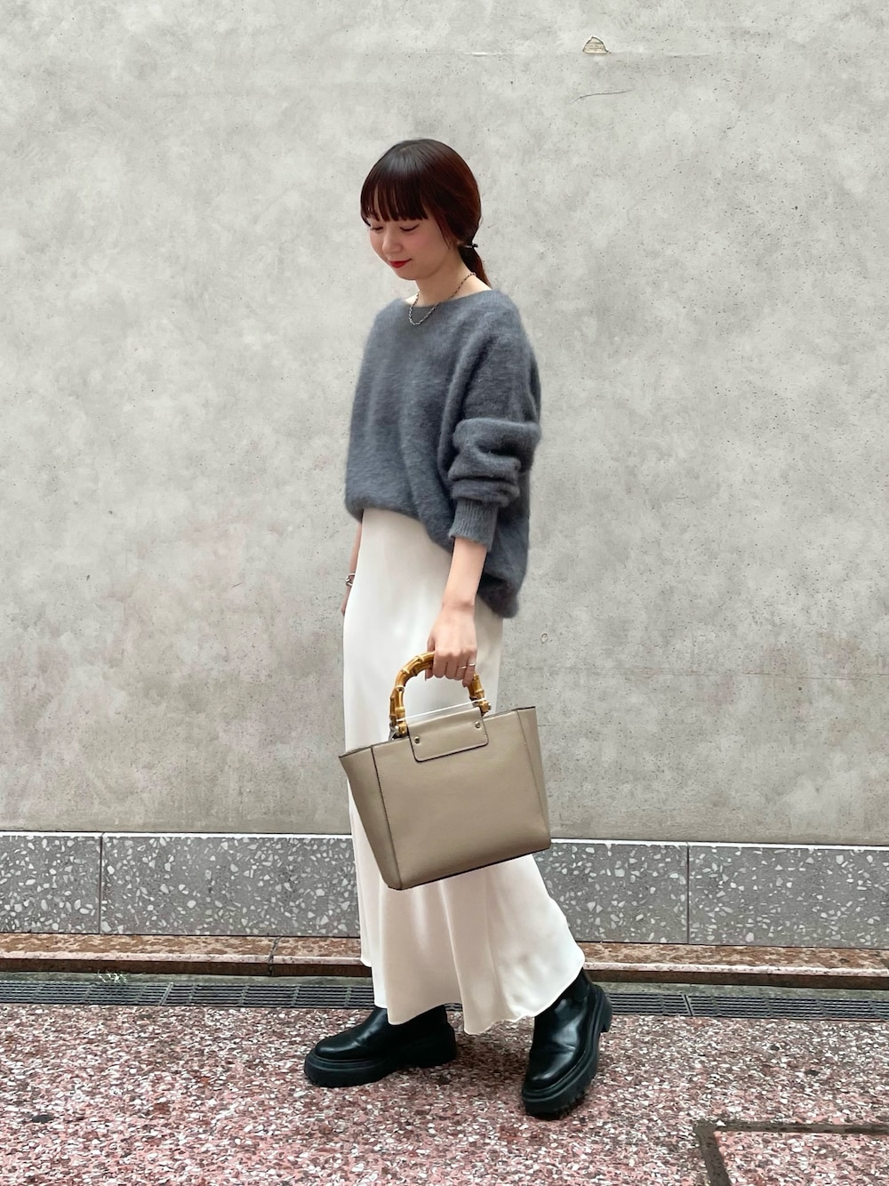 グレー系のニット/セーター、ホワイト系のスカート、ベージュ系のショルダーバッグを着用したレディースの秋コーディネートの1枚目の写真