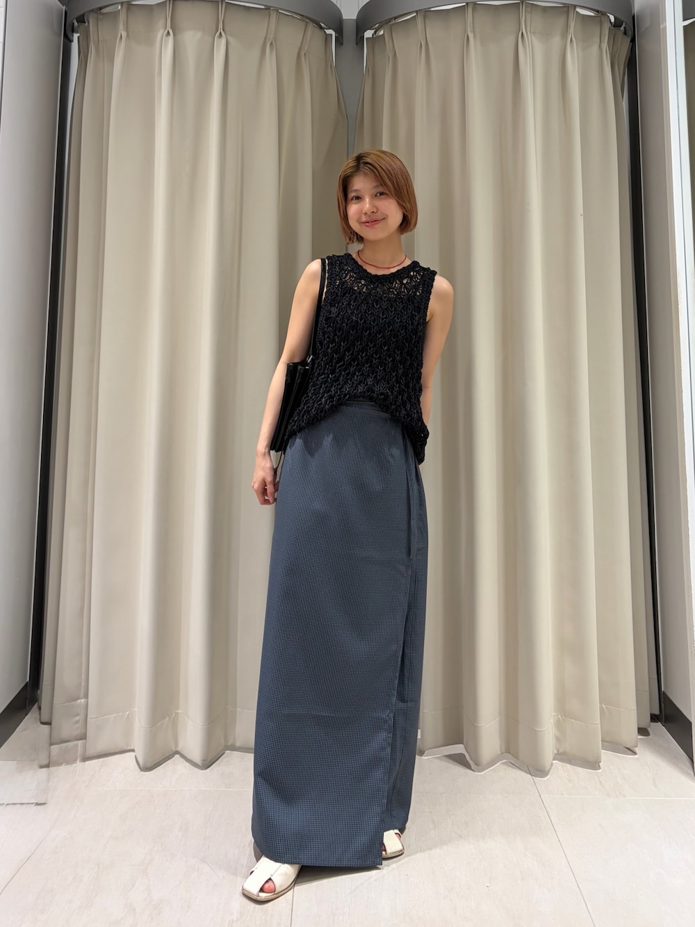 グレー系のスカート、ブラック系のニット/セーター、ブラック系のショルダーバッグを着用したレディースの夏コーディネートの1枚目の写真