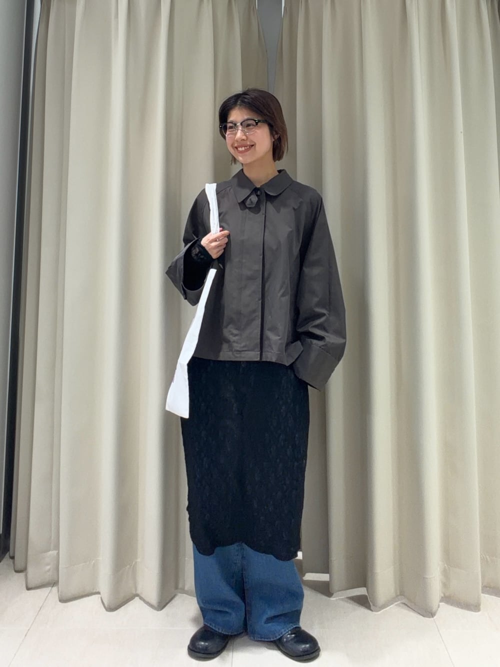 グレー系のステンカラーコート、ブラック系のワンピース、ブルー系のデニムパンツを着用したレディースの春コーディネートの1枚目の写真