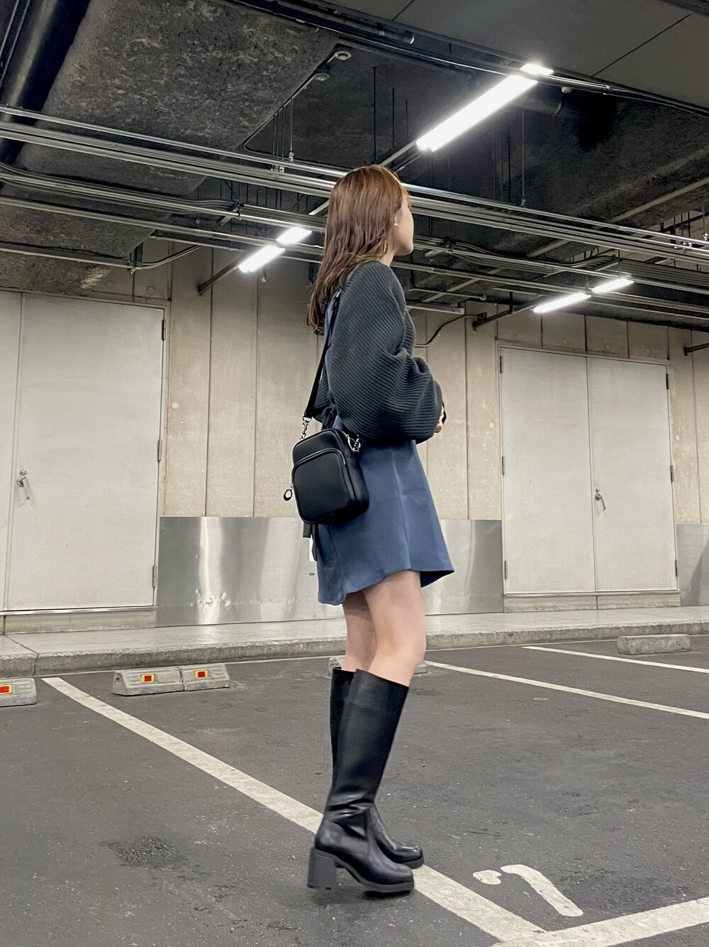 グレー系のワンピース、ブラック系のショルダーバッグ、ブラック系のブーツを着用したレディースの冬コーディネートの1枚目の写真