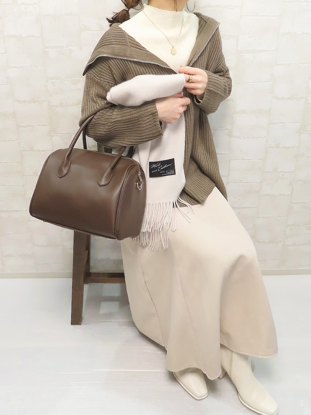 ブラウン系のニット/セーター、ブラウン系のボストンバッグ、ホワイト系のブーツを着用したレディースの冬コーディネートの1枚目の写真