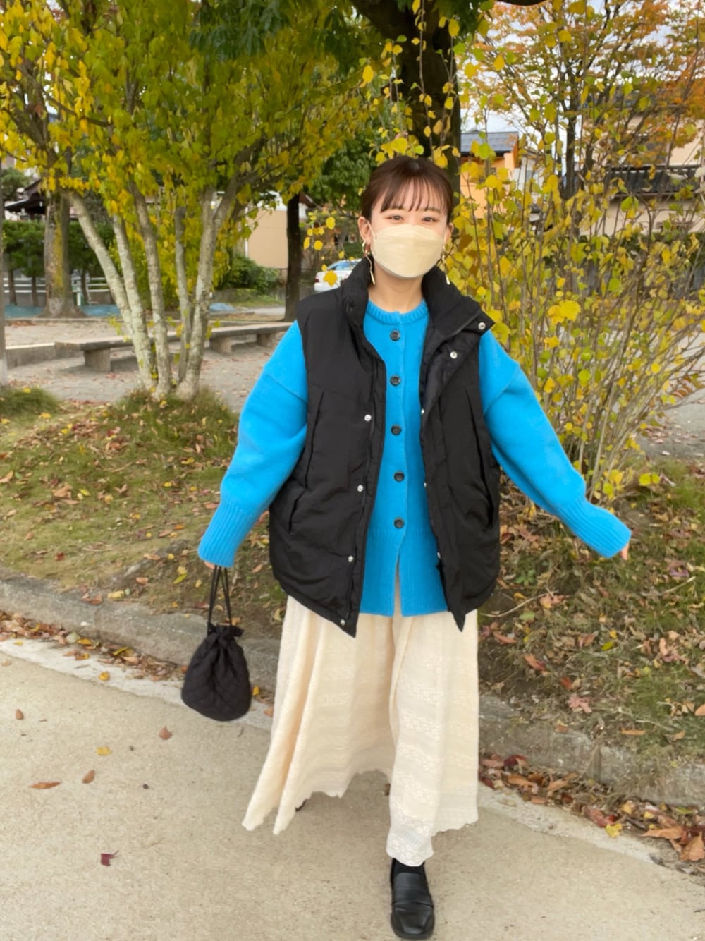 ベージュ系のスカート、ブルー系のカーディガン/ボレロ、ブラック系のダウンベストを着用したレディースの秋コーディネートの1枚目の写真