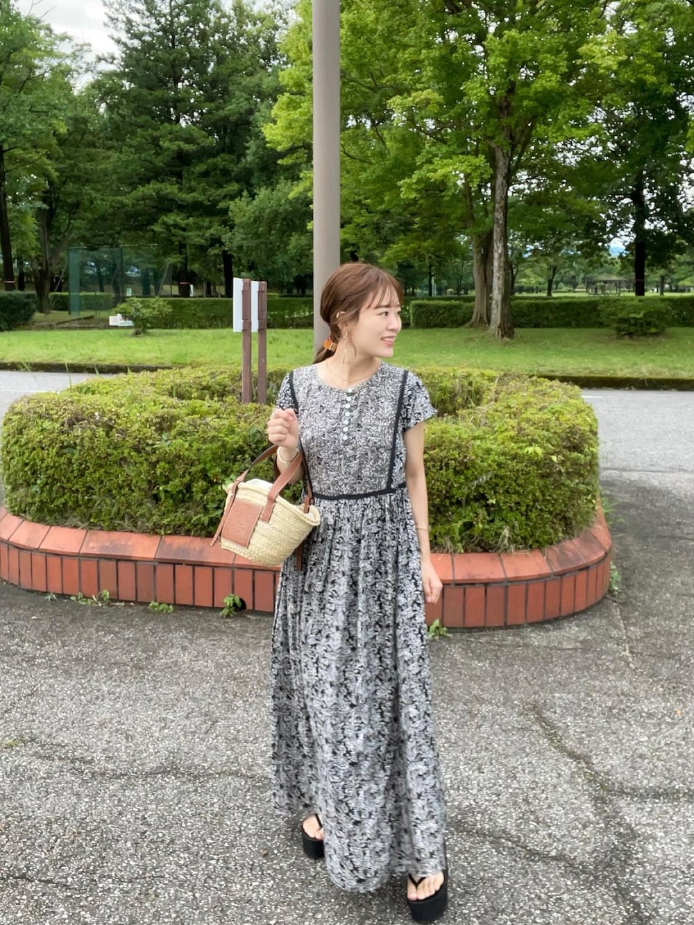 ブラック系のワンピース、ベージュ系のかごバッグ、ブラック系のサンダルを着用したレディースの夏コーディネートの1枚目の写真