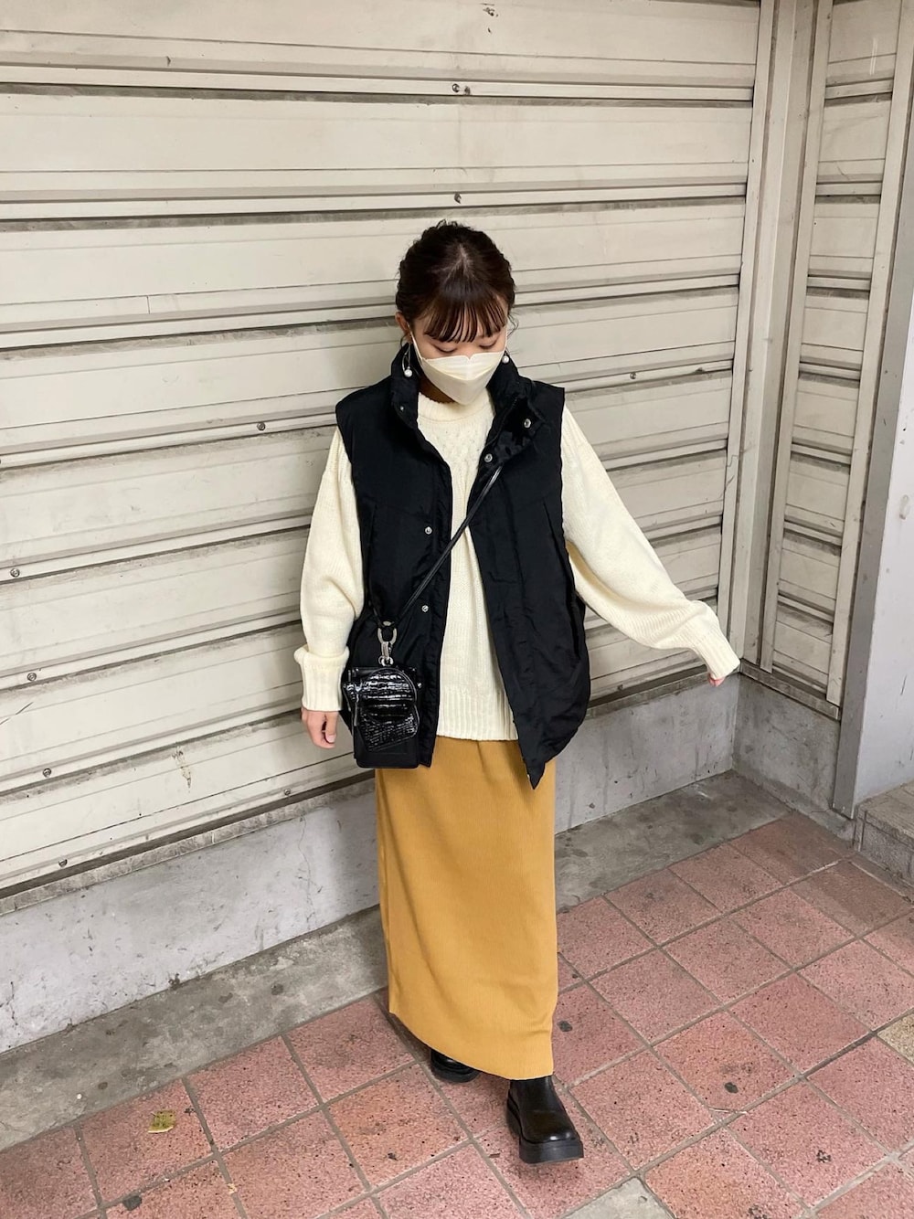 ホワイト系のニット/セーター、ブラック系のダウンベスト、イエロー系のスカートを着用したレディースの秋コーディネートの1枚目の写真