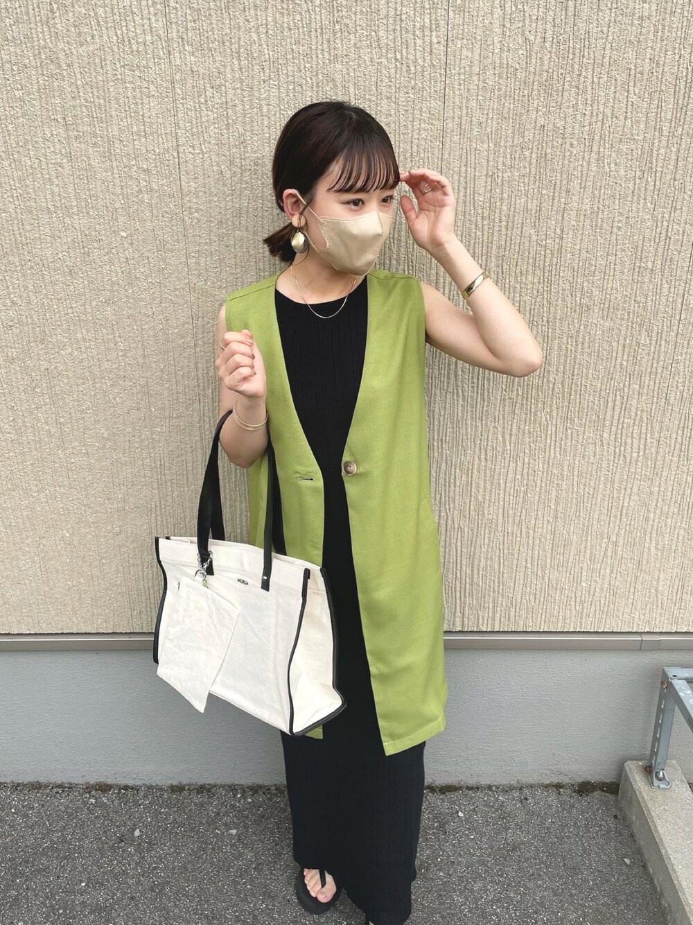 ホワイト系のトートバッグ、グリーン系のベスト、ブラック系のワンピースを着用したレディースの夏コーディネートの1枚目の写真