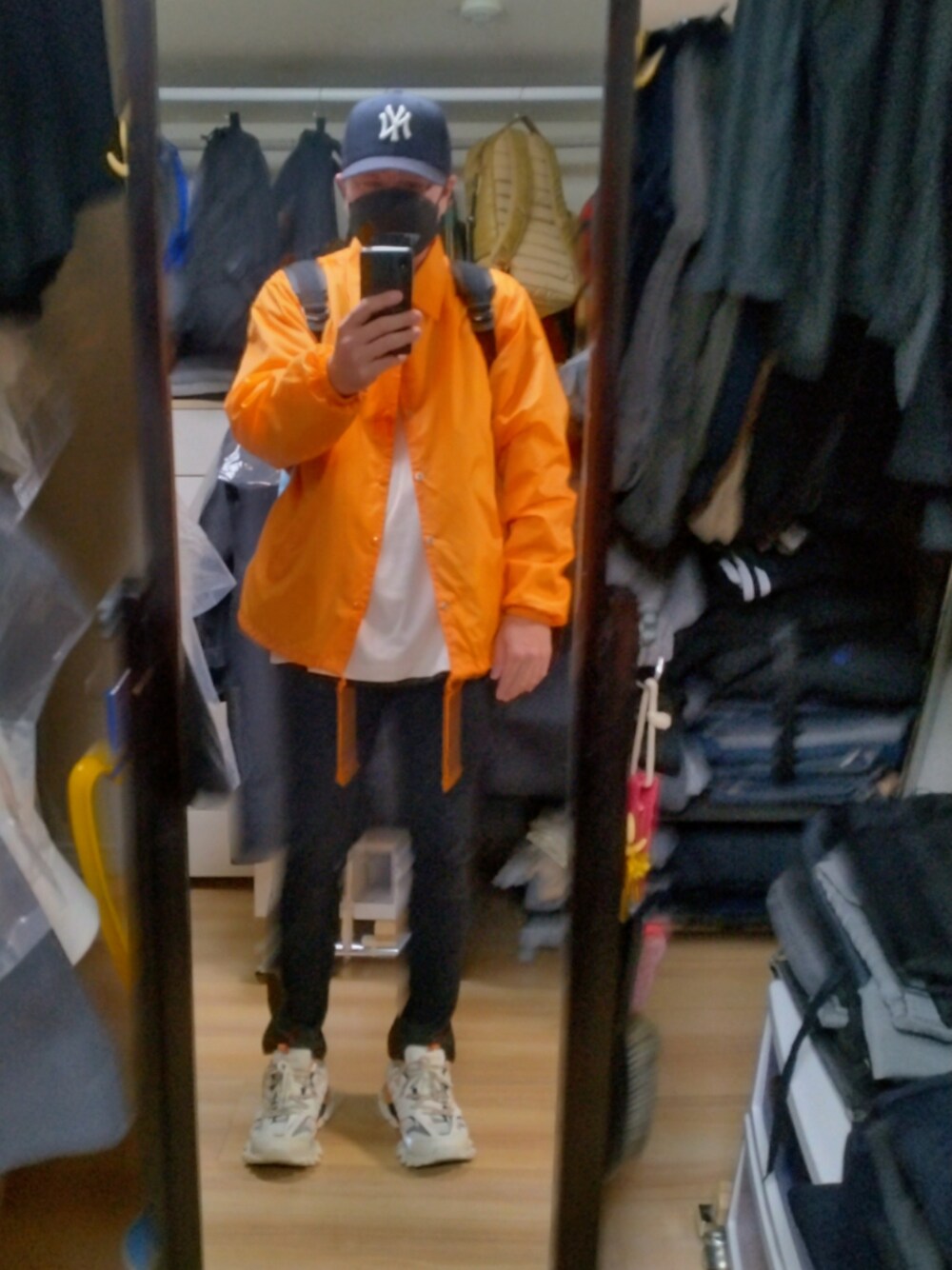 ホワイト系のスニーカー、ブラック系のその他パンツ、オレンジ系のナイロンジャケットを着用したメンズの春コーディネートの1枚目の写真