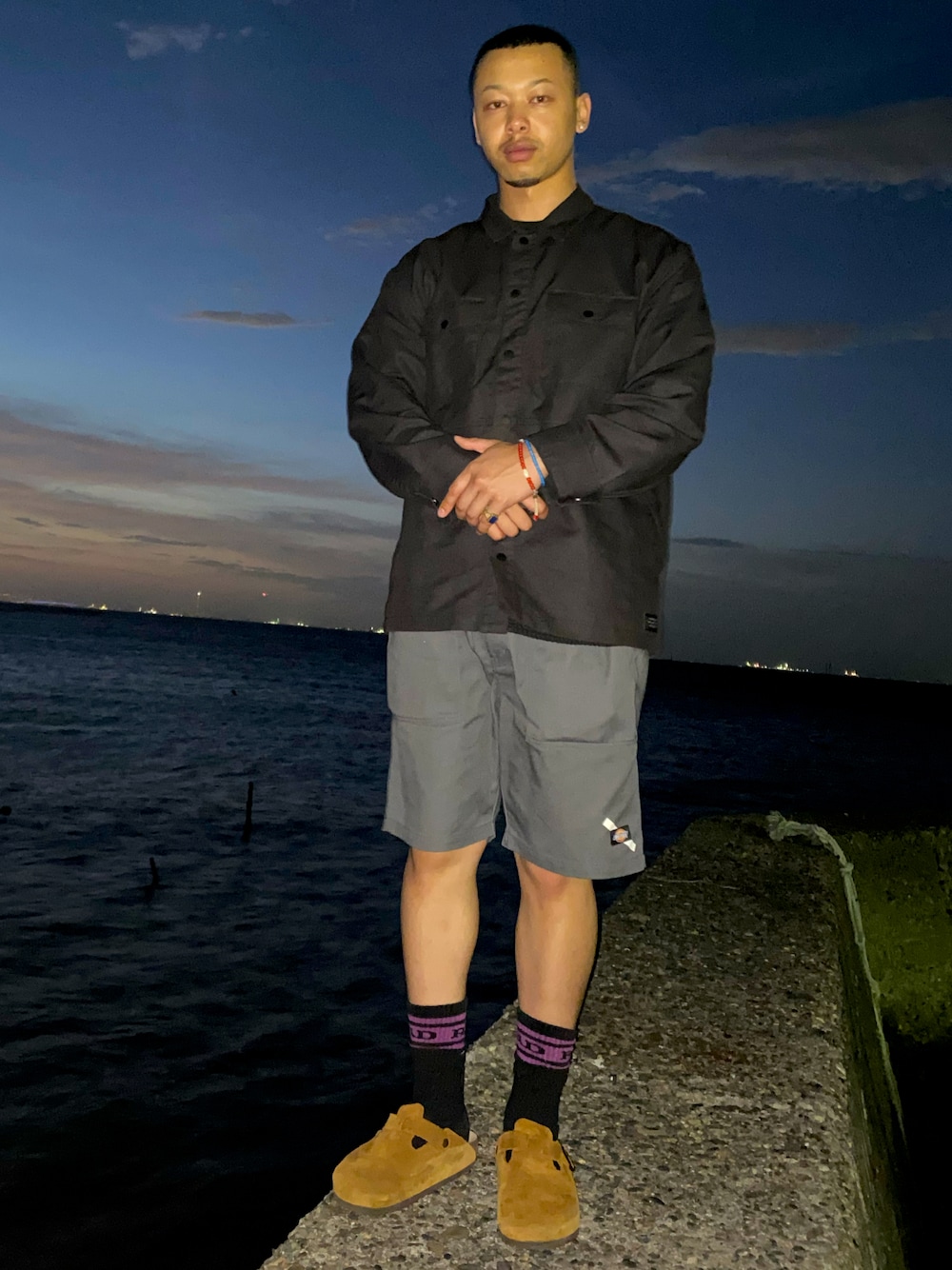 グレー系のチノパンツ、ブラック系のミリタリージャケットを着用したメンズの夏コーディネートの1枚目の写真