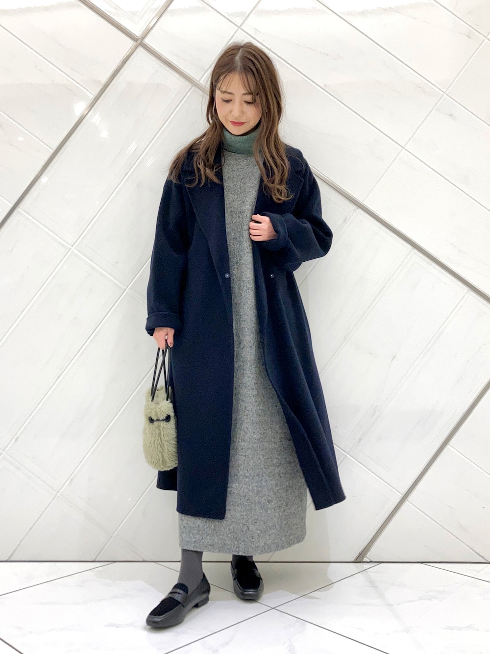 グリーン系のハンドバッグ、ブルー系のチェスターコート、ブラック系のローファーを着用したレディースの冬コーディネートの1枚目の写真