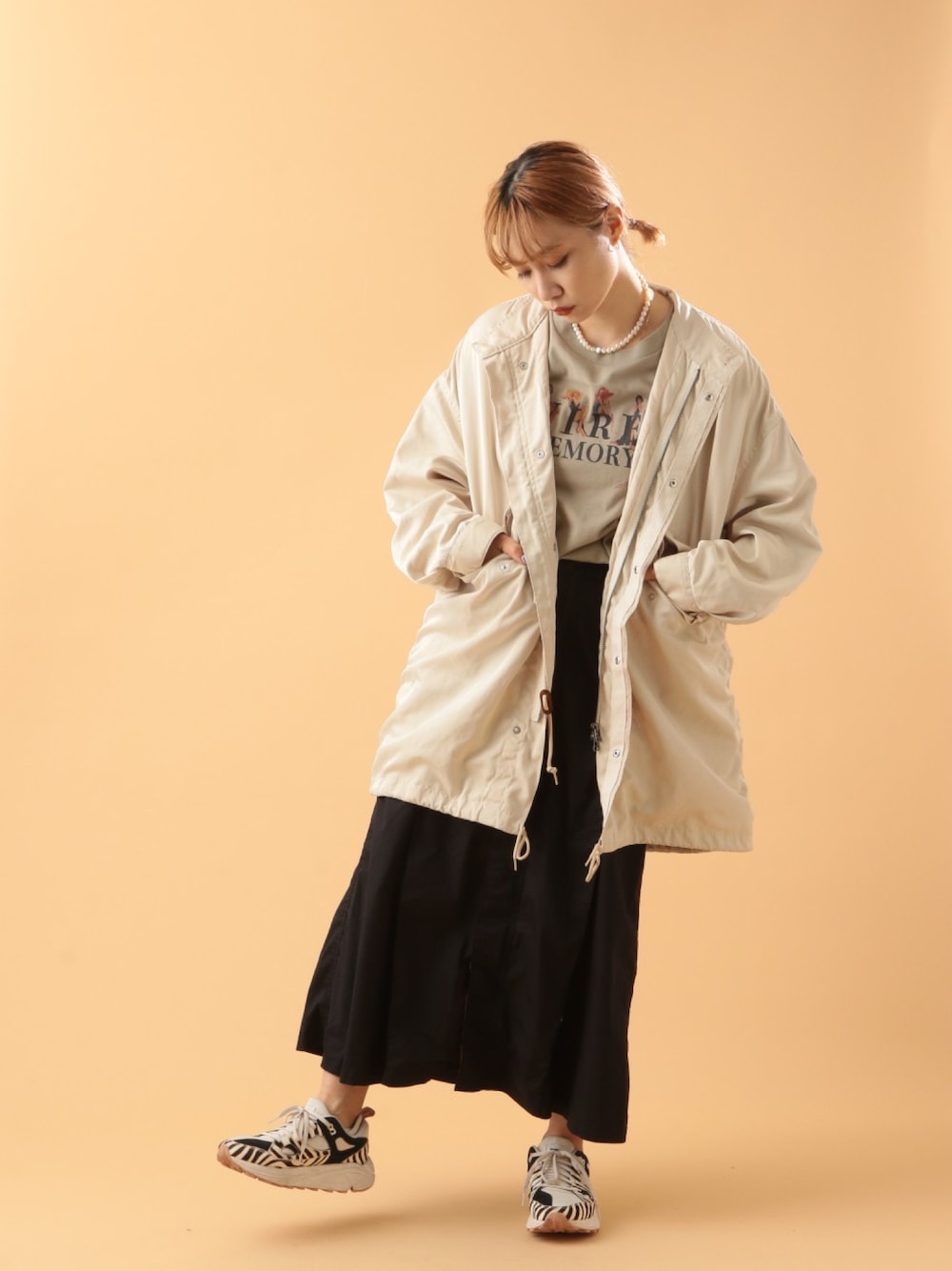 ホワイト系のミリタリージャケット、ベージュ系のTシャツ/カットソー、ブラック系のスカートを着用したレディースの冬コーディネートの1枚目の写真