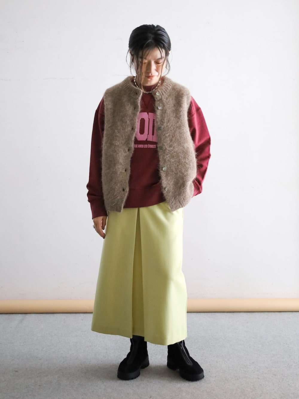 ブラウン系のベスト、レッド系のスウェット、イエロー系のスカートを着用したレディースの冬コーディネートの1枚目の写真
