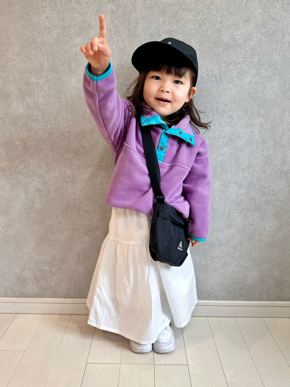 パープル系のスウェット、ホワイト系のスカート、ホワイト系のスニーカーを着用したキッズの冬コーディネートの1枚目の写真