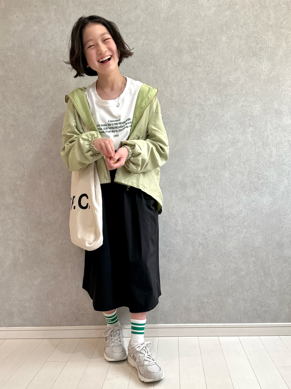 グリーン系のマウンテンパーカー、ホワイト系のTシャツ/カットソー、ブラック系のスカートを着用したキッズの春コーディネートの1枚目の写真