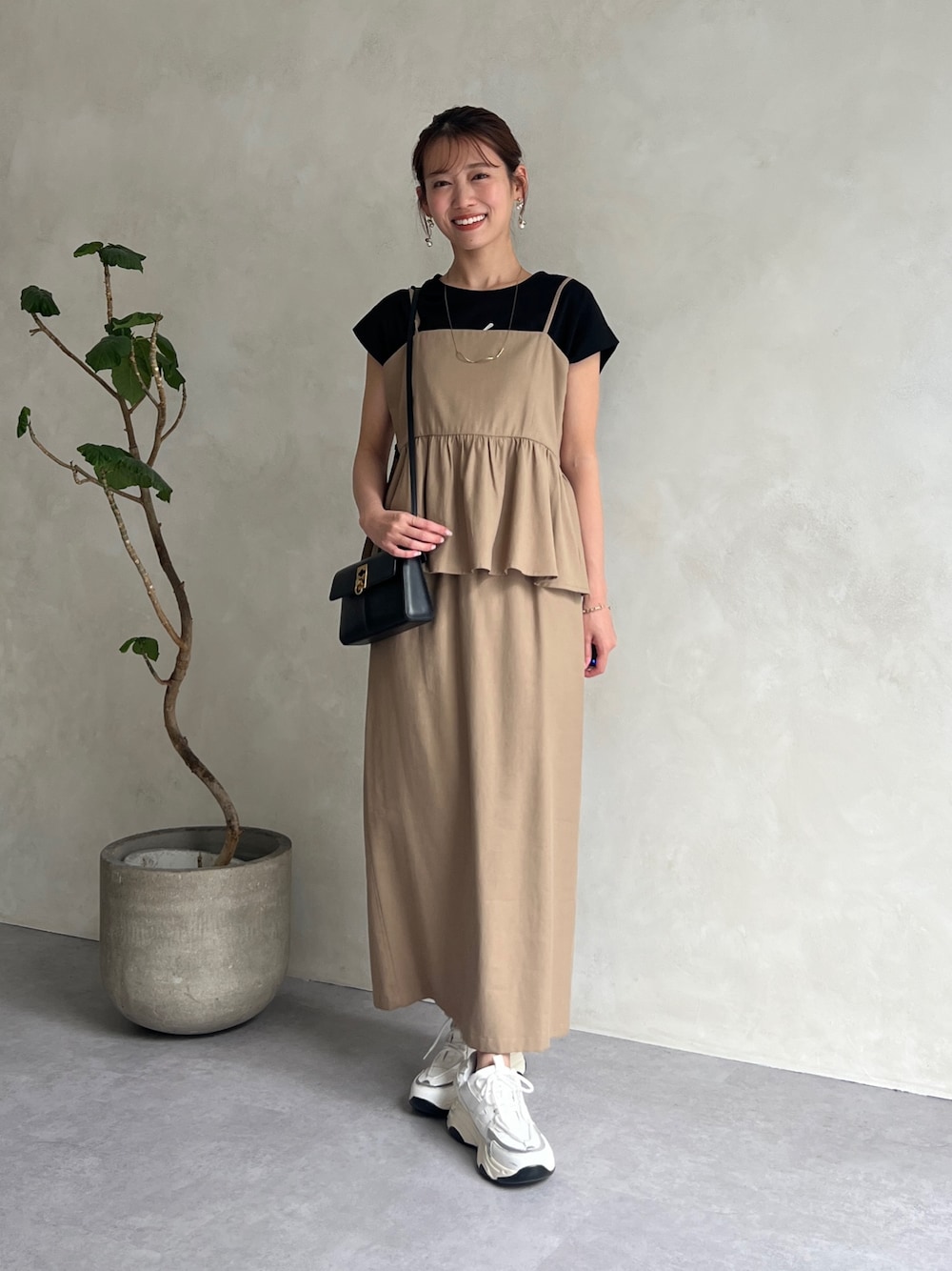 ベージュ系のワンピース、ブラック系のTシャツ/カットソー、ホワイト系のスニーカーを着用したレディースの夏コーディネートの1枚目の写真