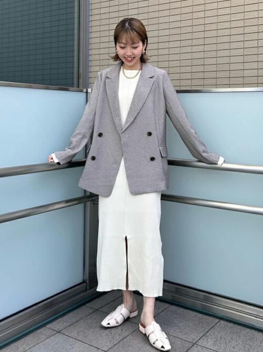 ベージュ系のテーラードジャケット、ホワイト系のワンピース、ホワイト系のサンダルを着用したレディースの冬コーディネートの1枚目の写真
