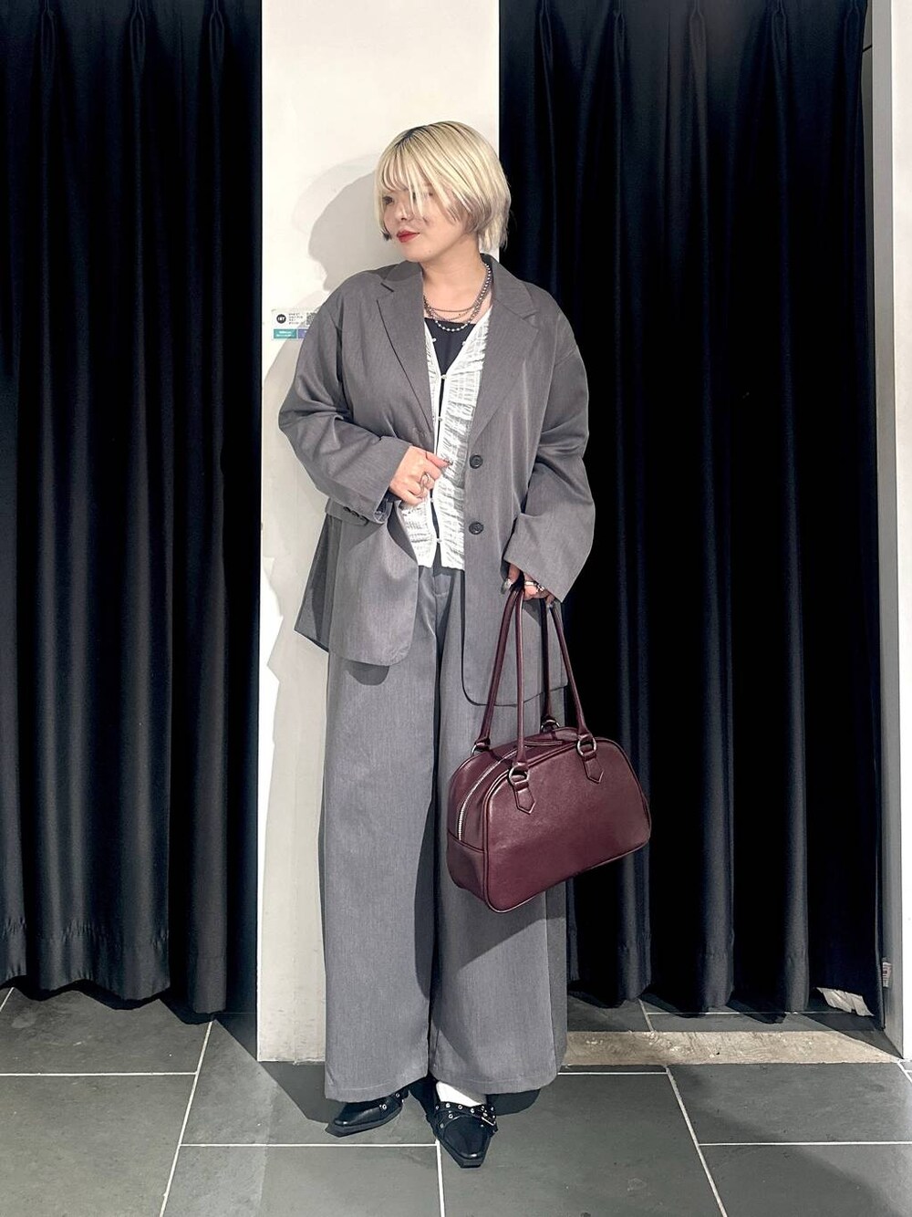 グレー系のテーラードジャケット、グレー系のスラックス、レッド系のボストンバッグを着用したレディースの秋コーディネートの1枚目の写真