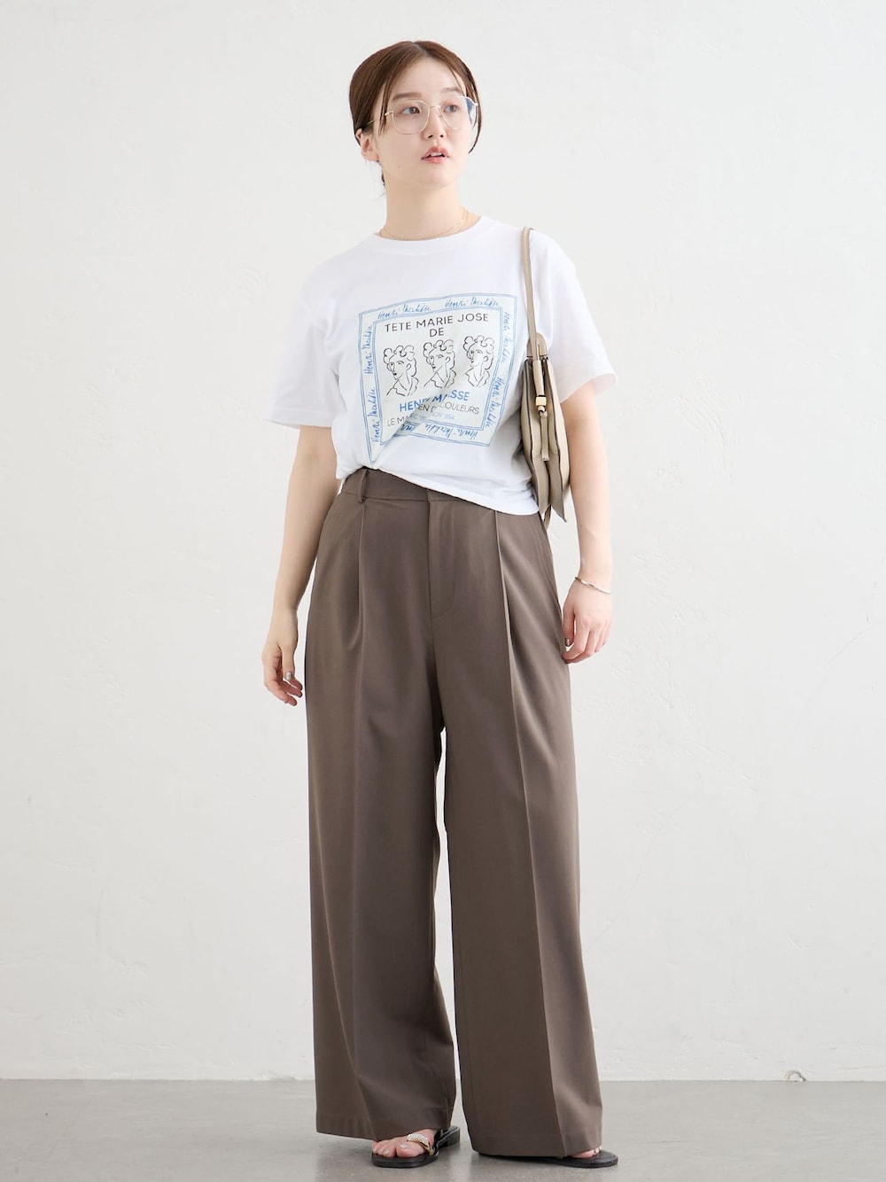 ブラウン系のスラックス、ホワイト系のTシャツ/カットソー、ブラック系のサンダルを着用したレディースの夏コーディネートの1枚目の写真