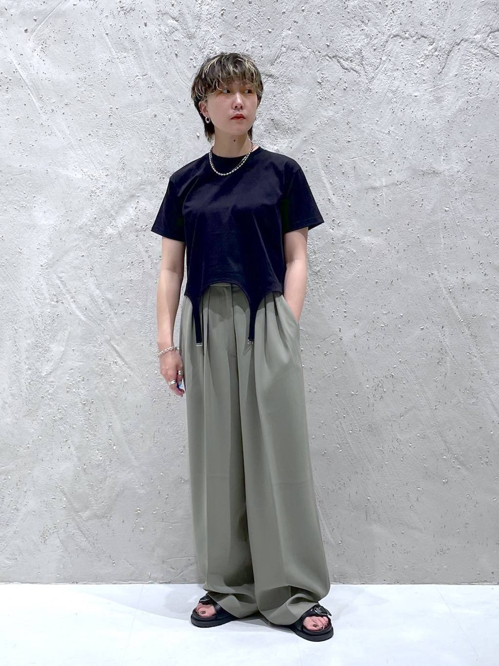 グリーン系のスラックス、ブラック系のTシャツ/カットソー、ブラック系のサンダルを着用したレディースの夏コーディネートの1枚目の写真