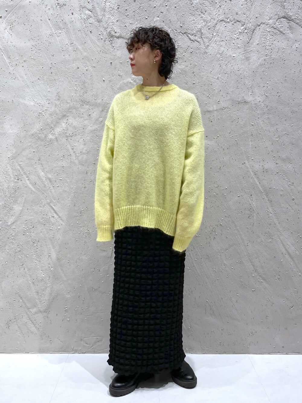 イエロー系のニット/セーター、ブラック系のスカート、ブラック系のブーツを着用したレディースの冬コーディネートの1枚目の写真