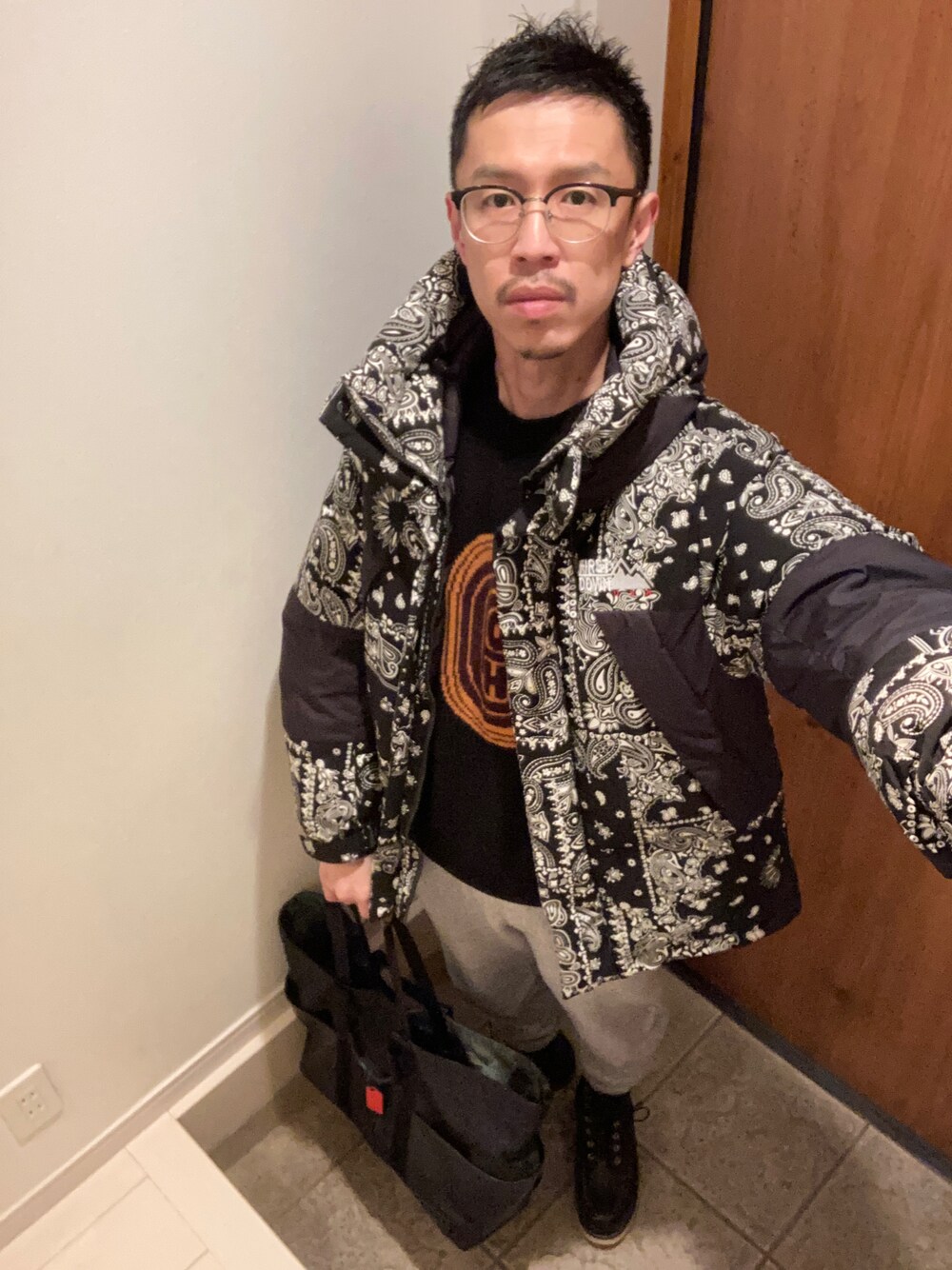 ブラック系のダウンジャケット/コート、ブラック系のニット/セーター、ブラック系のトートバッグを着用したメンズの冬コーディネートの1枚目の写真