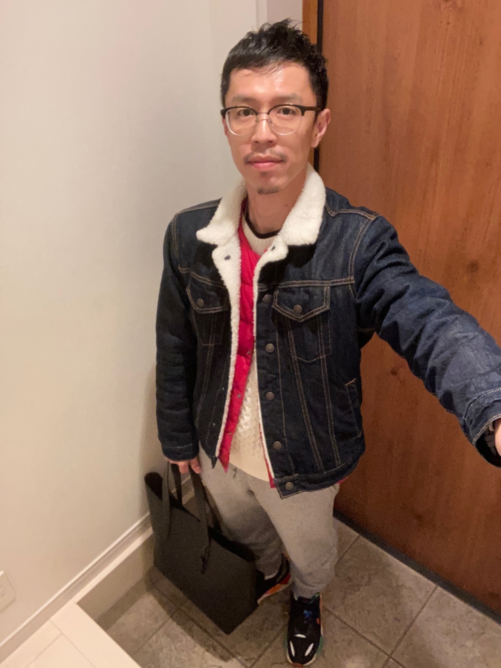 ベージュ系のニット/セーター、ブルー系のデニムジャケット、オレンジ系のダウンベストを着用したメンズの冬コーディネートの1枚目の写真