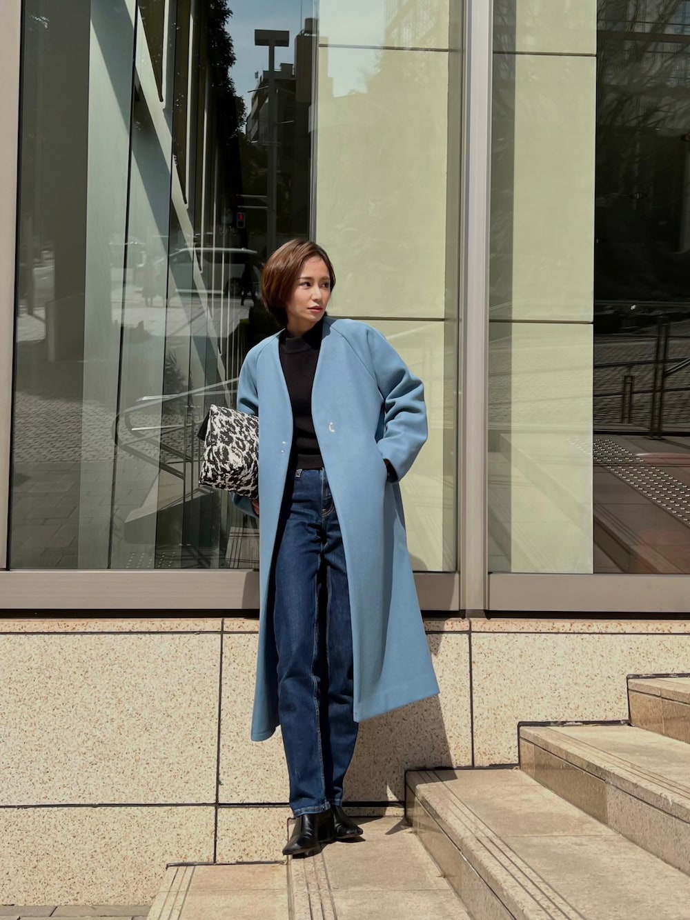 ブルー系のノーカラーコート、ブラック系のハンドバッグを着用したレディースの春コーディネートの1枚目の写真