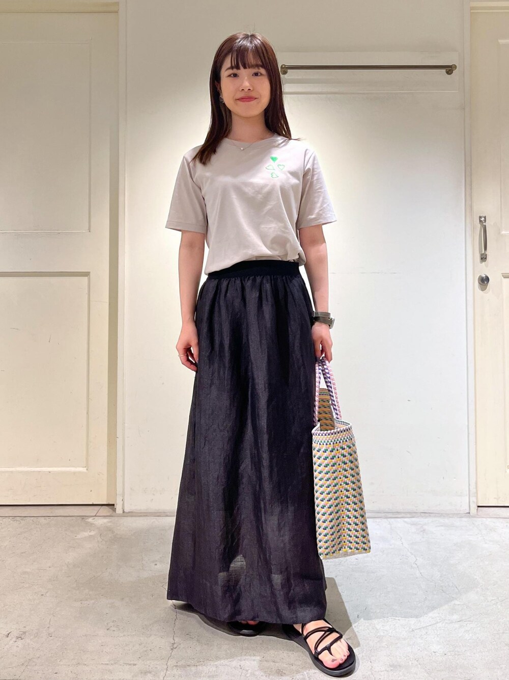 ブラック系のスカート、ベージュ系のTシャツ/カットソーを着用したレディースの夏コーディネートの1枚目の写真