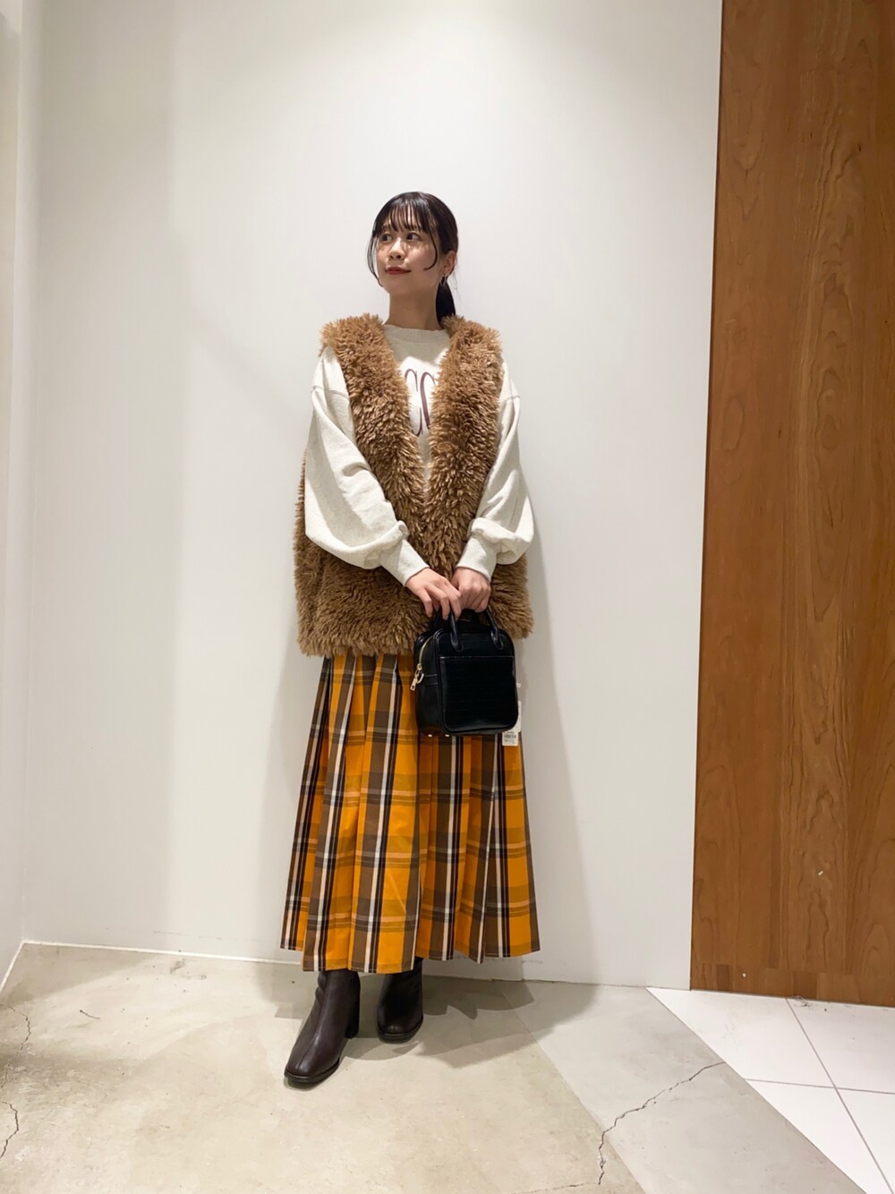 オレンジ系のスカート、ブラウン系のブーツ、ブラック系のボストンバッグを着用したレディースの秋コーディネートの1枚目の写真