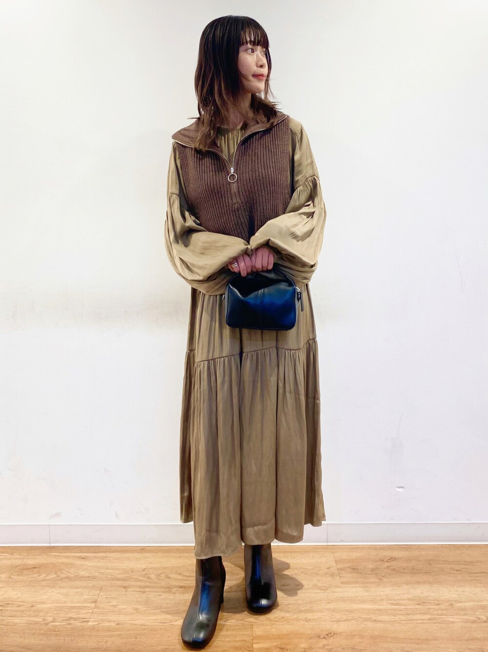 ブラック系のショルダーバッグ、ブラウン系のベスト、ベージュ系のワンピースを着用したレディースの秋コーディネートの1枚目の写真