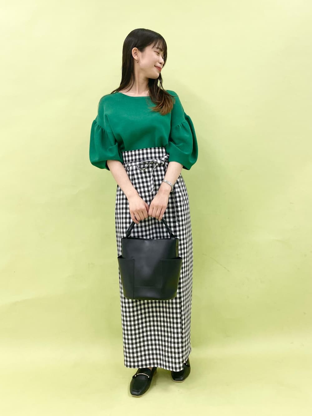 グリーン系のニット/セーター、ブラック系のスカート、ブラック系のローファーを着用したレディースの夏コーディネートの1枚目の写真