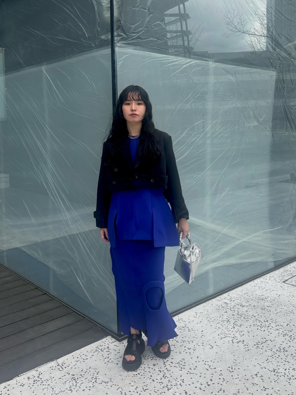 ブラック系のテーラードジャケット、ブルー系のニット/セーター、ブルー系のスカートを着用したレディースの春コーディネートの1枚目の写真