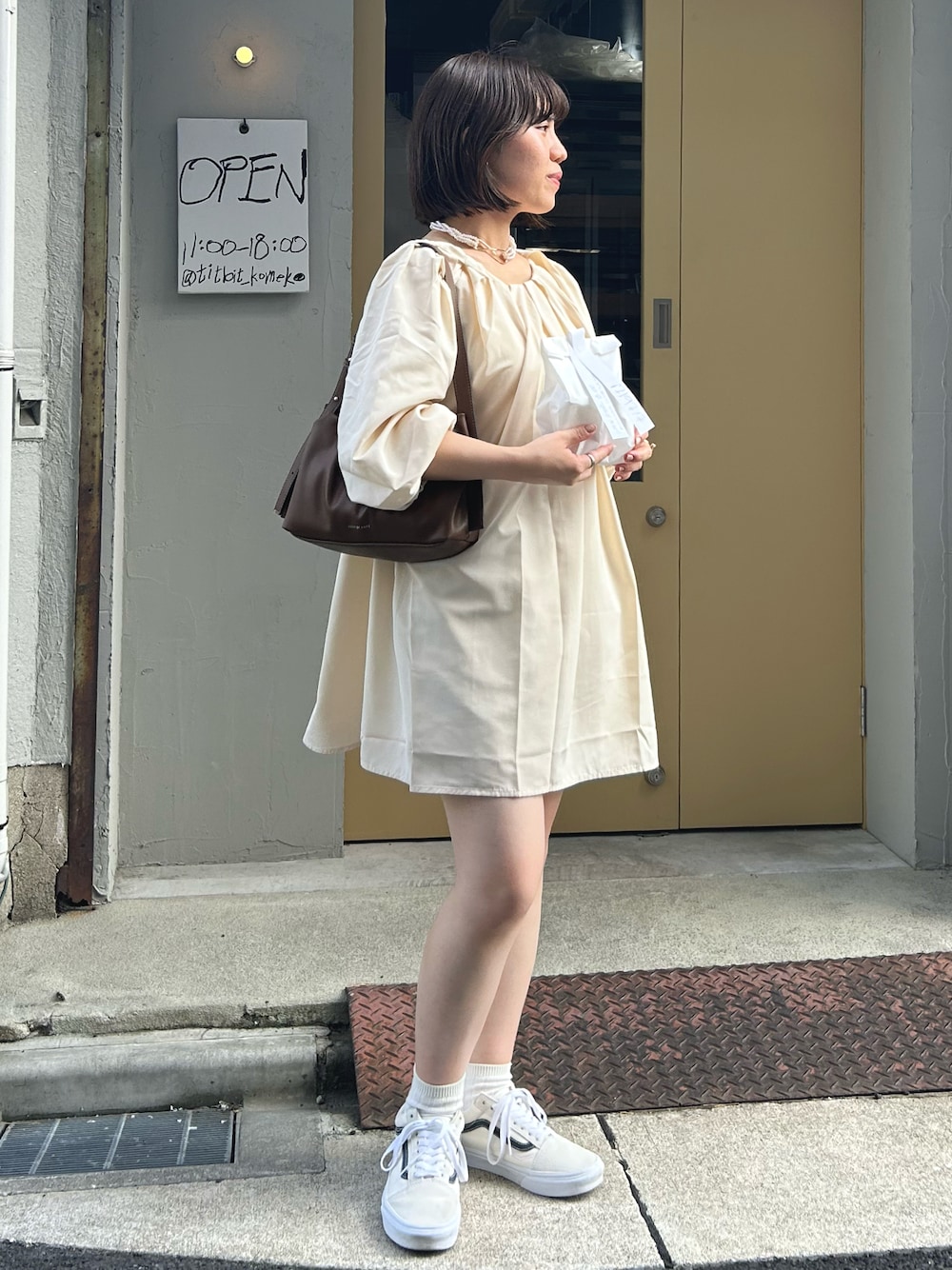 ホワイト系のスニーカー、ブラウン系のトートバッグ、ベージュ系のシャツ/ブラウスを着用したレディースの秋コーディネートの1枚目の写真
