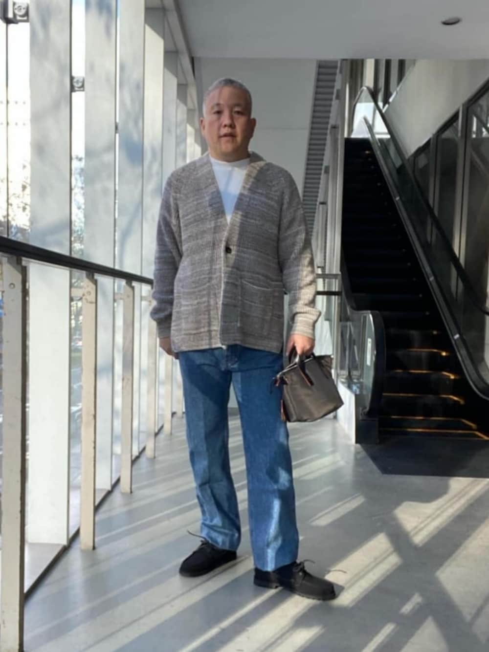 ホワイト系のTシャツ/カットソー、ブルー系のデニムパンツ、ブラウン系のトートバッグを着用したメンズの冬コーディネートの1枚目の写真