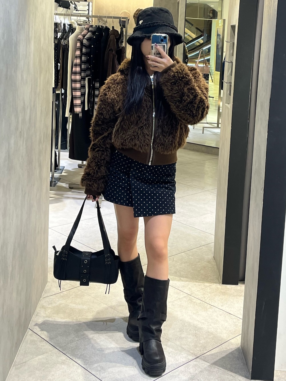 ブラック系のブーツ、ブラック系のハンドバッグ、ブルー系のスカートを着用したレディースの秋コーディネートの1枚目の写真