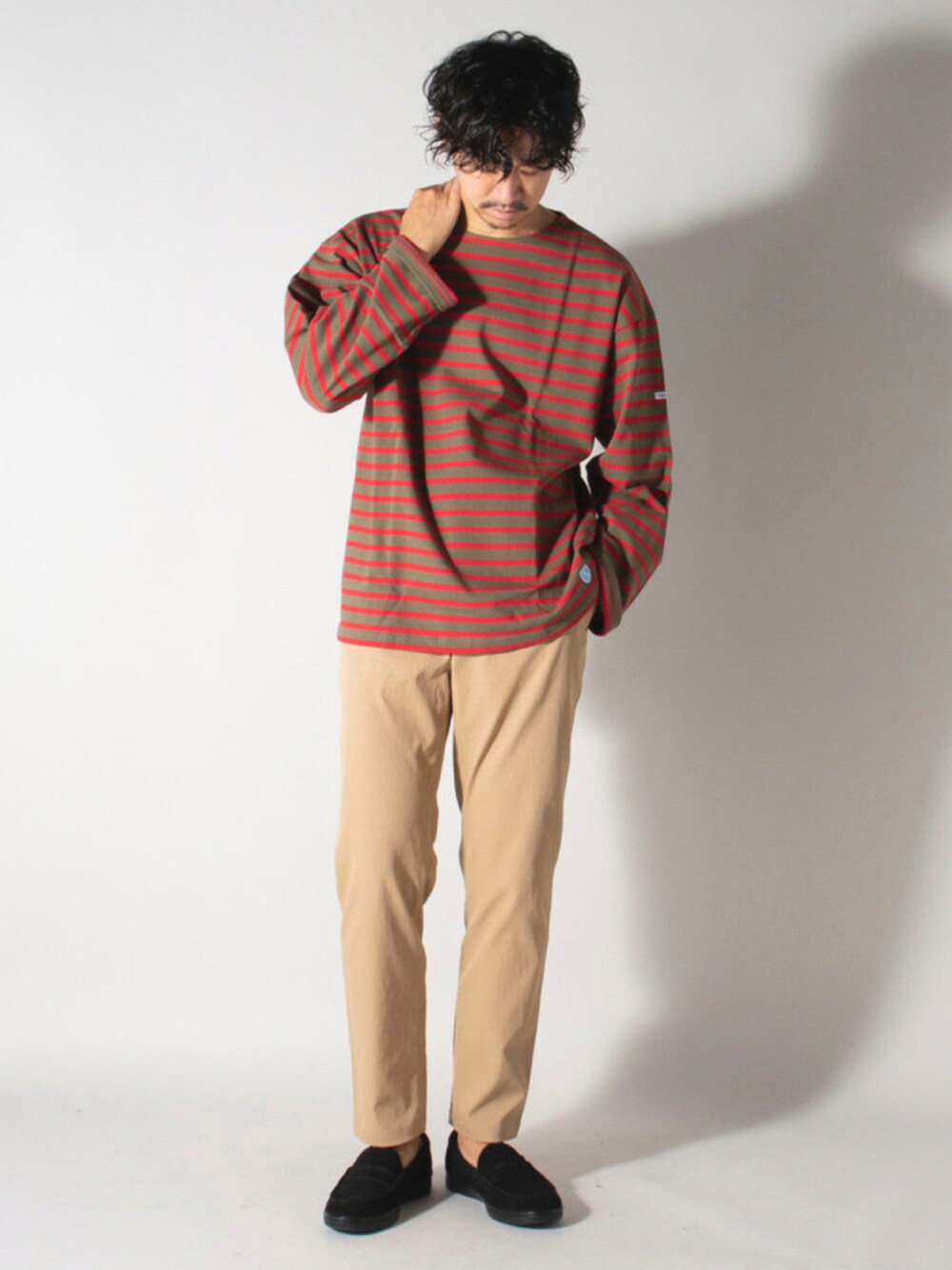 レッド系のTシャツ/カットソー、ベージュ系のスラックス、ブラック系のローファーを着用したメンズの秋コーディネートの1枚目の写真