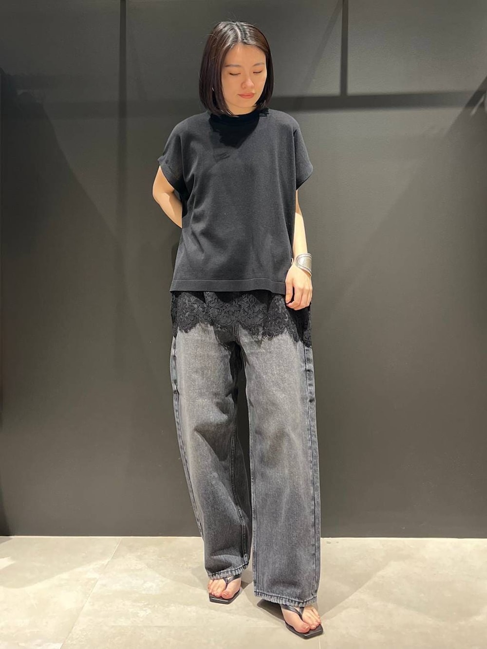 ブラック系のデニムパンツ、ブラック系のニット/セーター、シルバー系のバングル/リストバンドを着用したレディースの春コーディネートの1枚目の写真