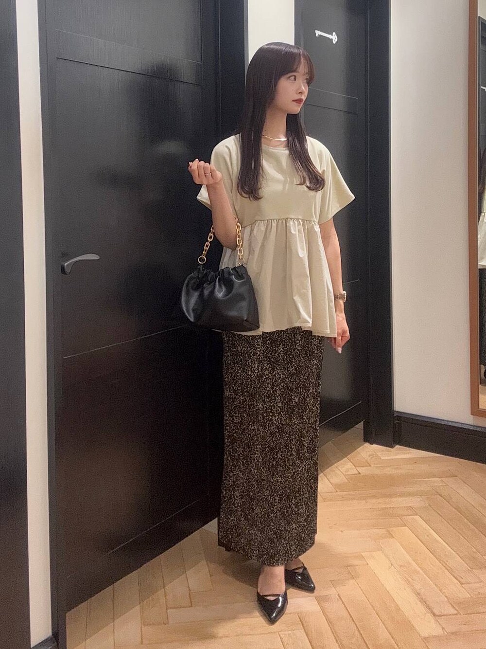 ブラウン系のスカート、ブラック系のパンプス、ブラック系のショルダーバッグを着用したレディースの夏コーディネートの1枚目の写真