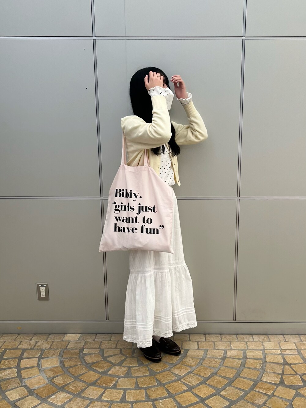 ピンク系のトートバッグ、ホワイト系のカーディガン/ボレロ、ホワイト系のTシャツ/カットソーを着用したレディースの春コーディネートの1枚目の写真