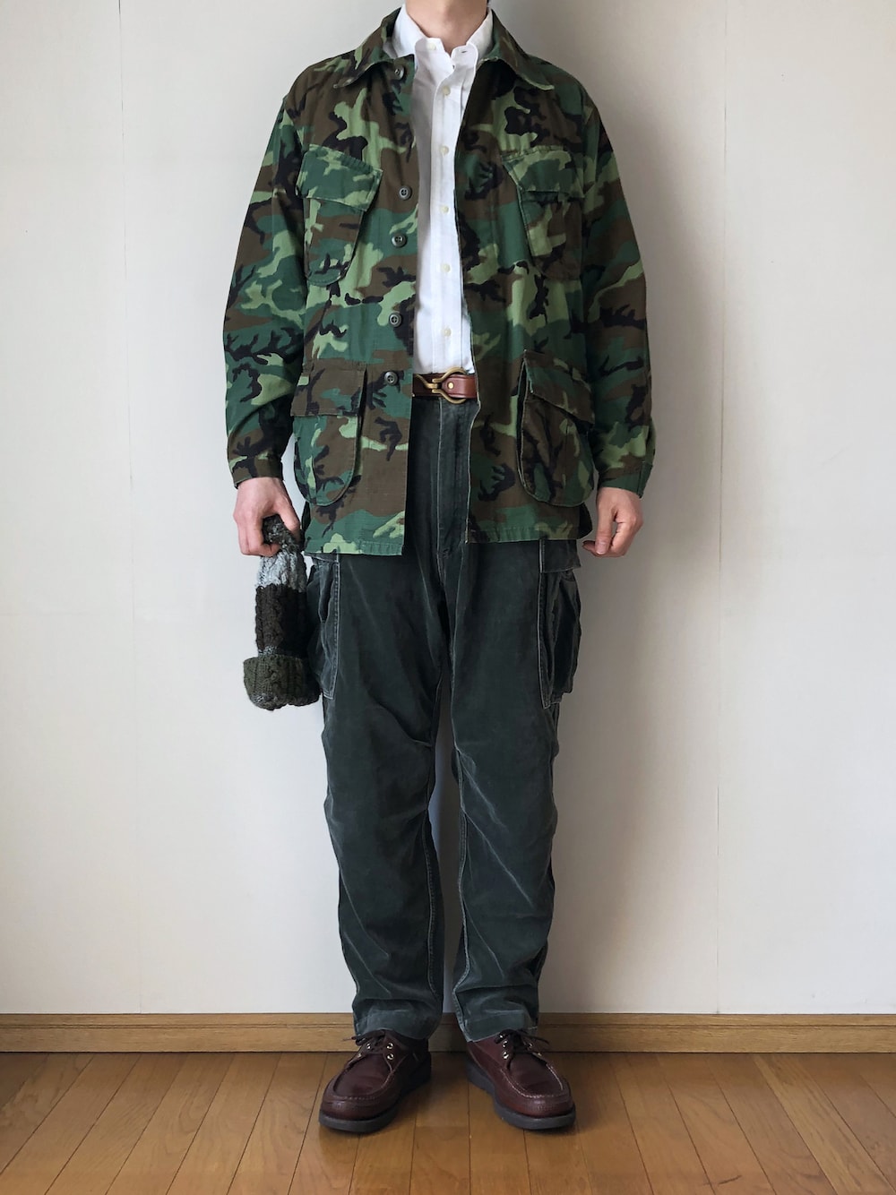 「ジャングルファティーグ、JUNGLEFATIGUE、ミリタリー、ミリタリージャケット、カモフラ、ボタンダウンシャツ、白シャツ、タックイン、カーゴパンツ、ベロアパンツ、ニット帽、ポンポン帽子、ケーブルニット、モカシン、ブーツ」｜「MILITARYのJUNGLE FATIGUE JACKET（ミリタリージャケット、グリーン系）」を使った、となりさん（メンズ・179cm）の春コーディネートの1枚目の写真