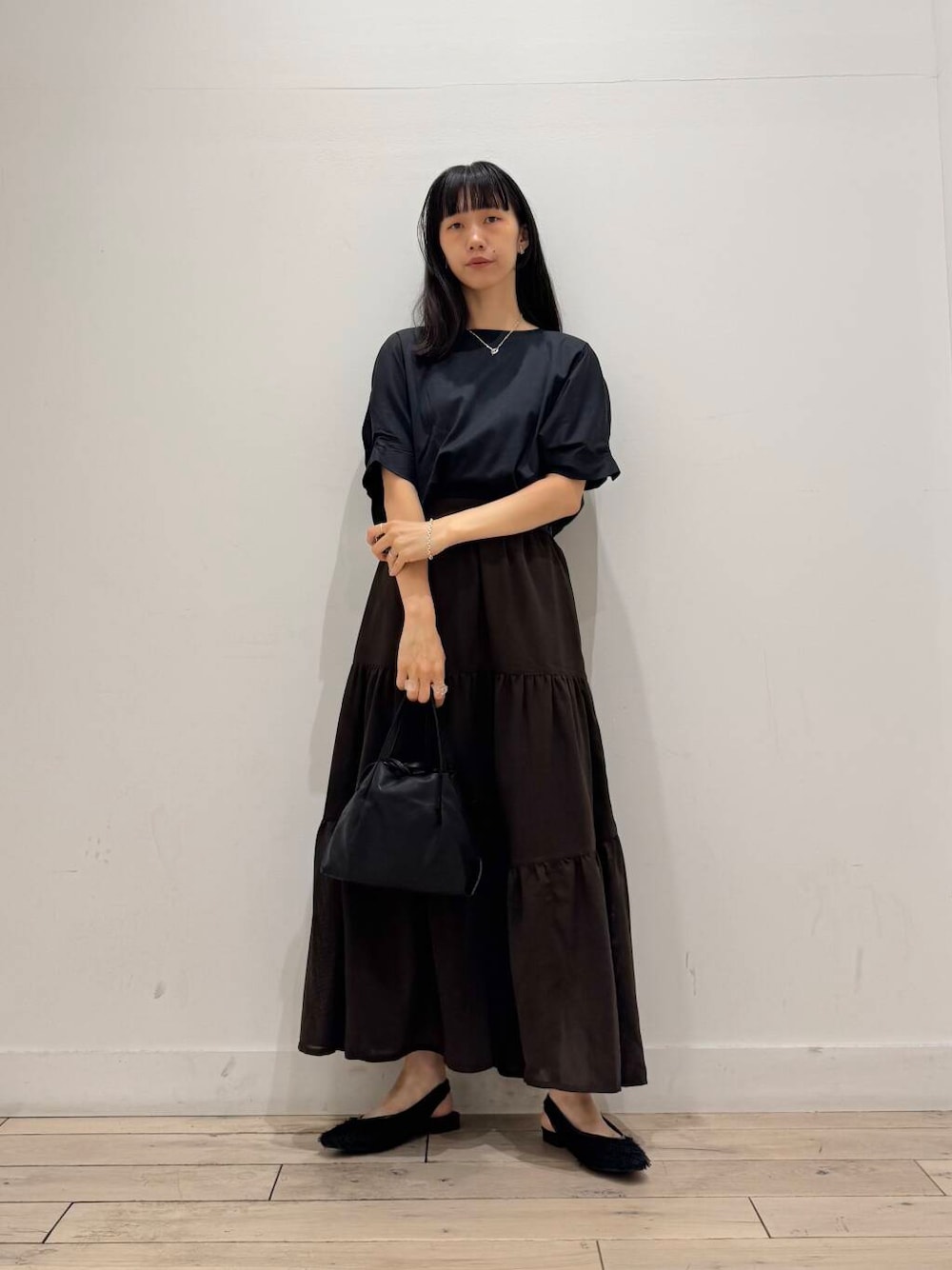 ブラック系のショルダーバッグ、ブラック系のTシャツ/カットソー、ブラウン系のスカートを着用したレディースの夏コーディネートの1枚目の写真