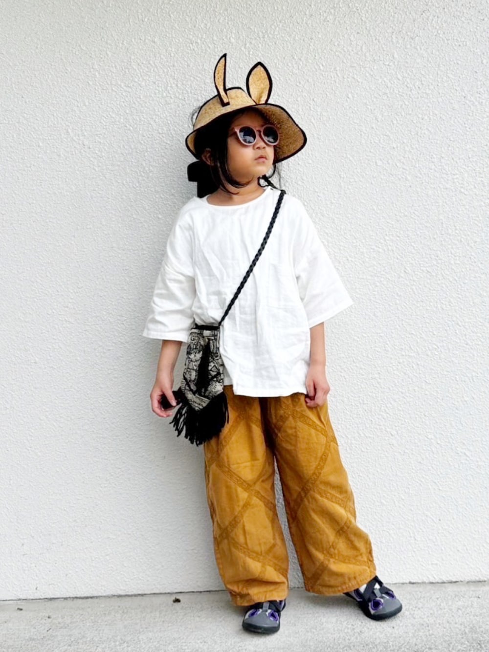 ホワイト系のトップス、ベージュ系のパンツ、ブラック系のバッグを着用したキッズの夏コーディネートの1枚目の写真